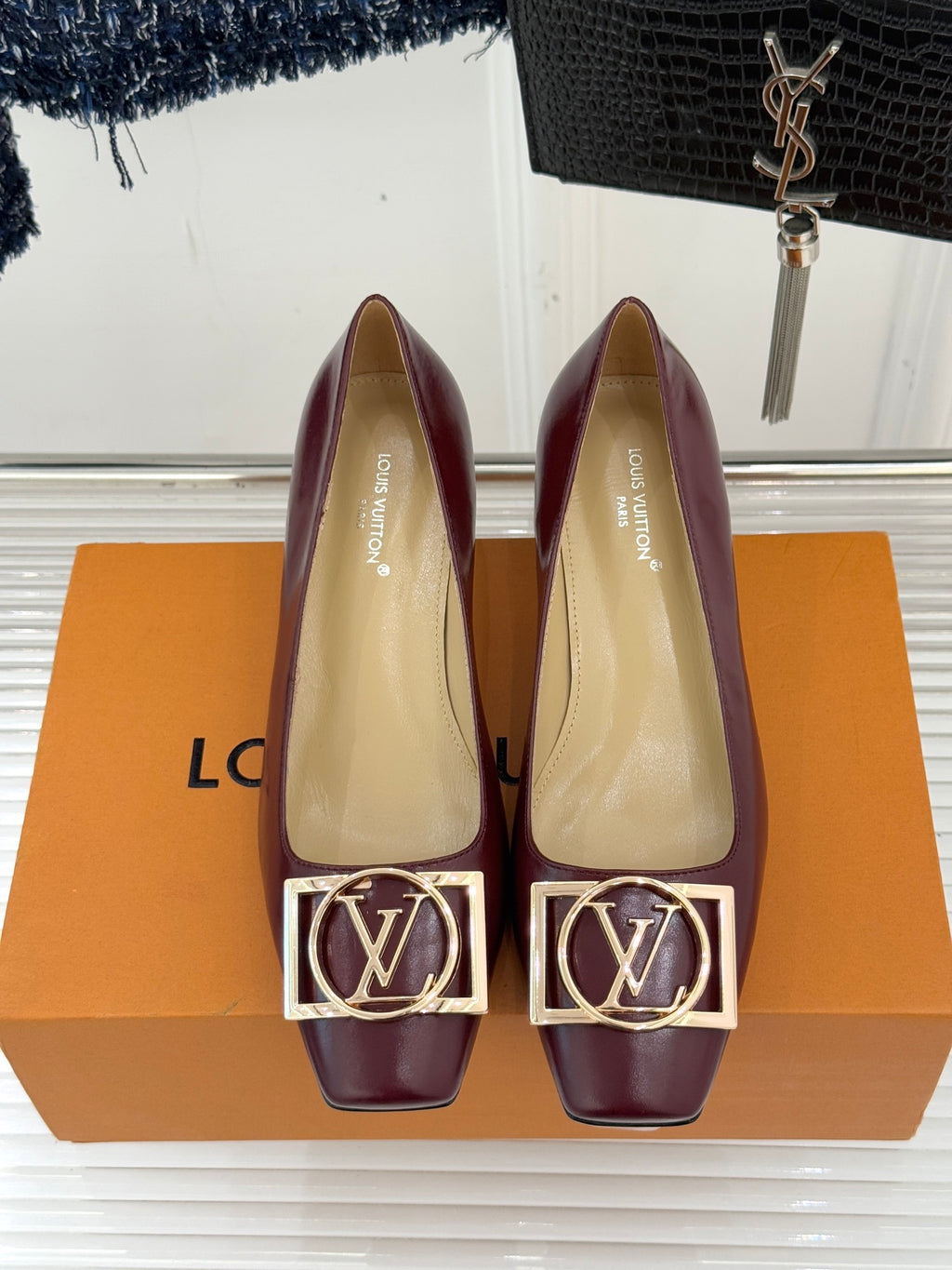 Burgundy low-heel pumps with gold square logo buckle detail, pointed toe.