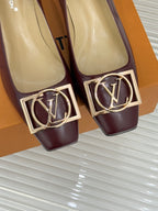 Close-up of burgundy low-heel pumps with gold square logo buckle detail.