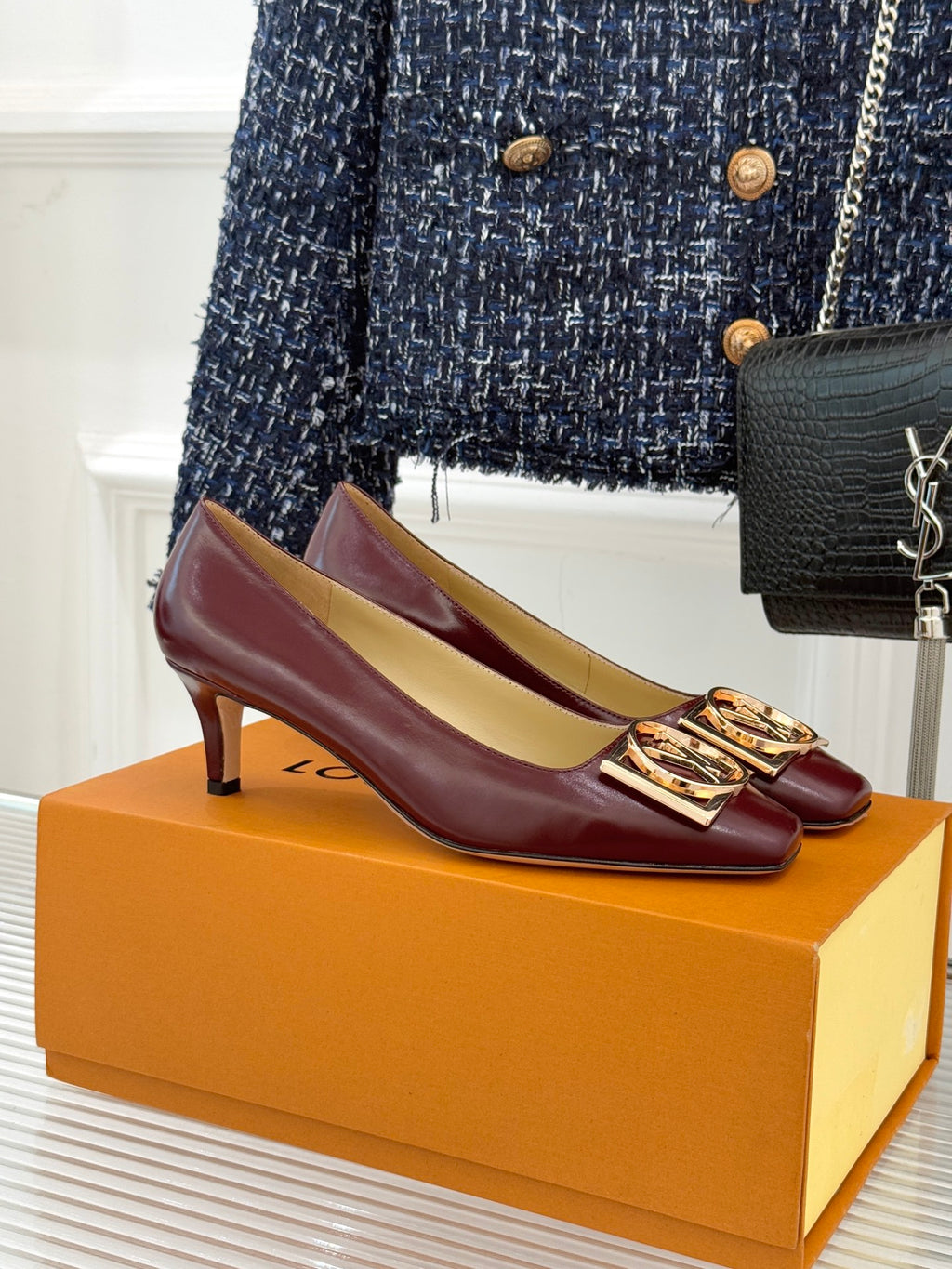 Burgundy leather low-heel pumps with gold logo square buckle detail.