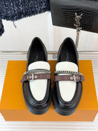 Front view of black loafers with white top panels, chain trim, and monogram strap