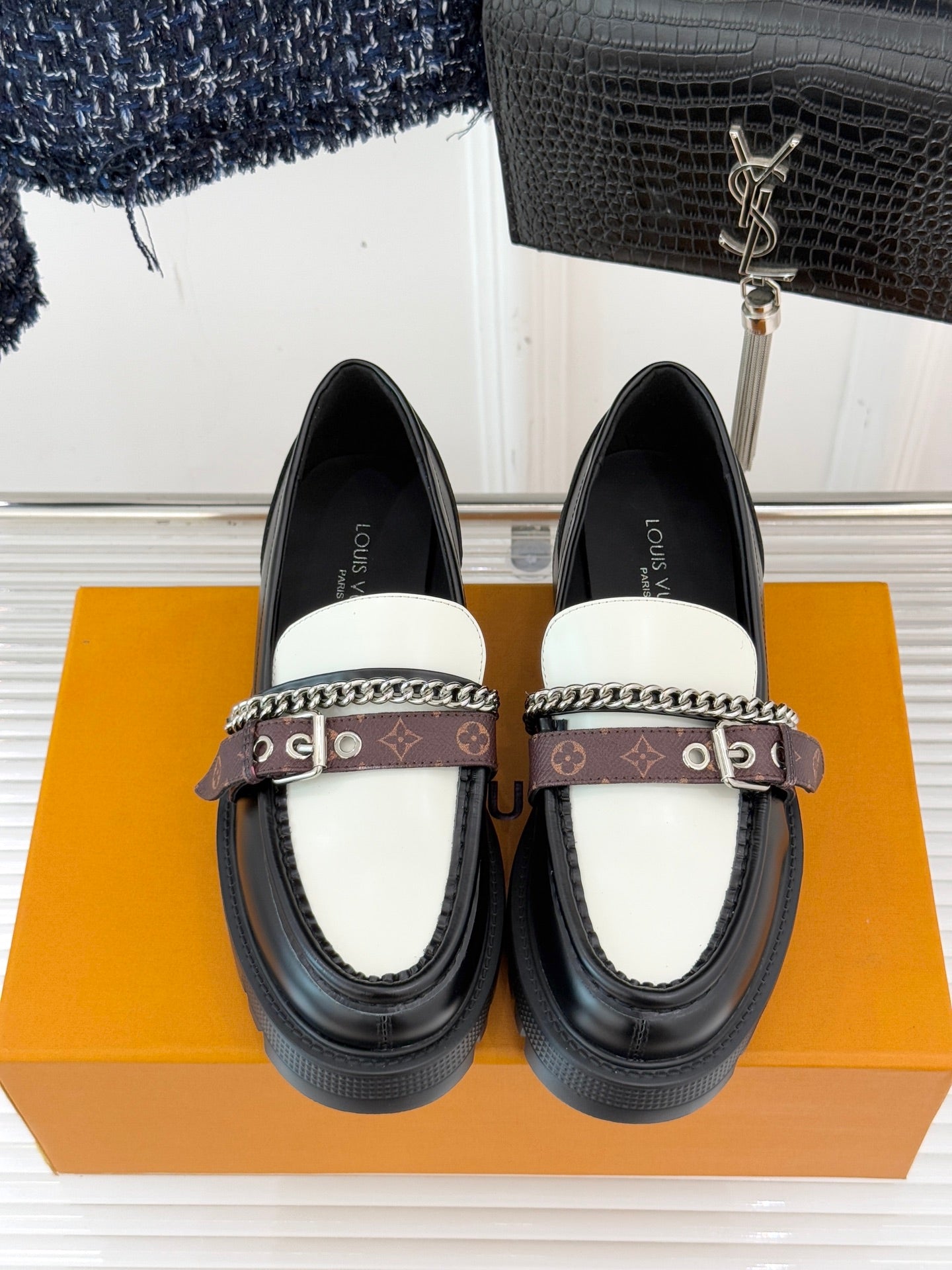 Front view of black loafers with white top panels, chain trim, and monogram strap