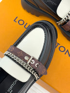 Close-up of black loafer with white panel, chain strap, and monogram buckle detail