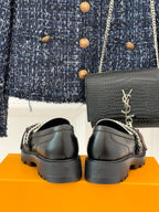 Back view of black loafers on orange box, with chunky sole and metal logo charm