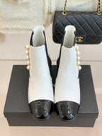 Pair of white ankle boots with black elastic sides, pearl accents, and glossy black toe caps