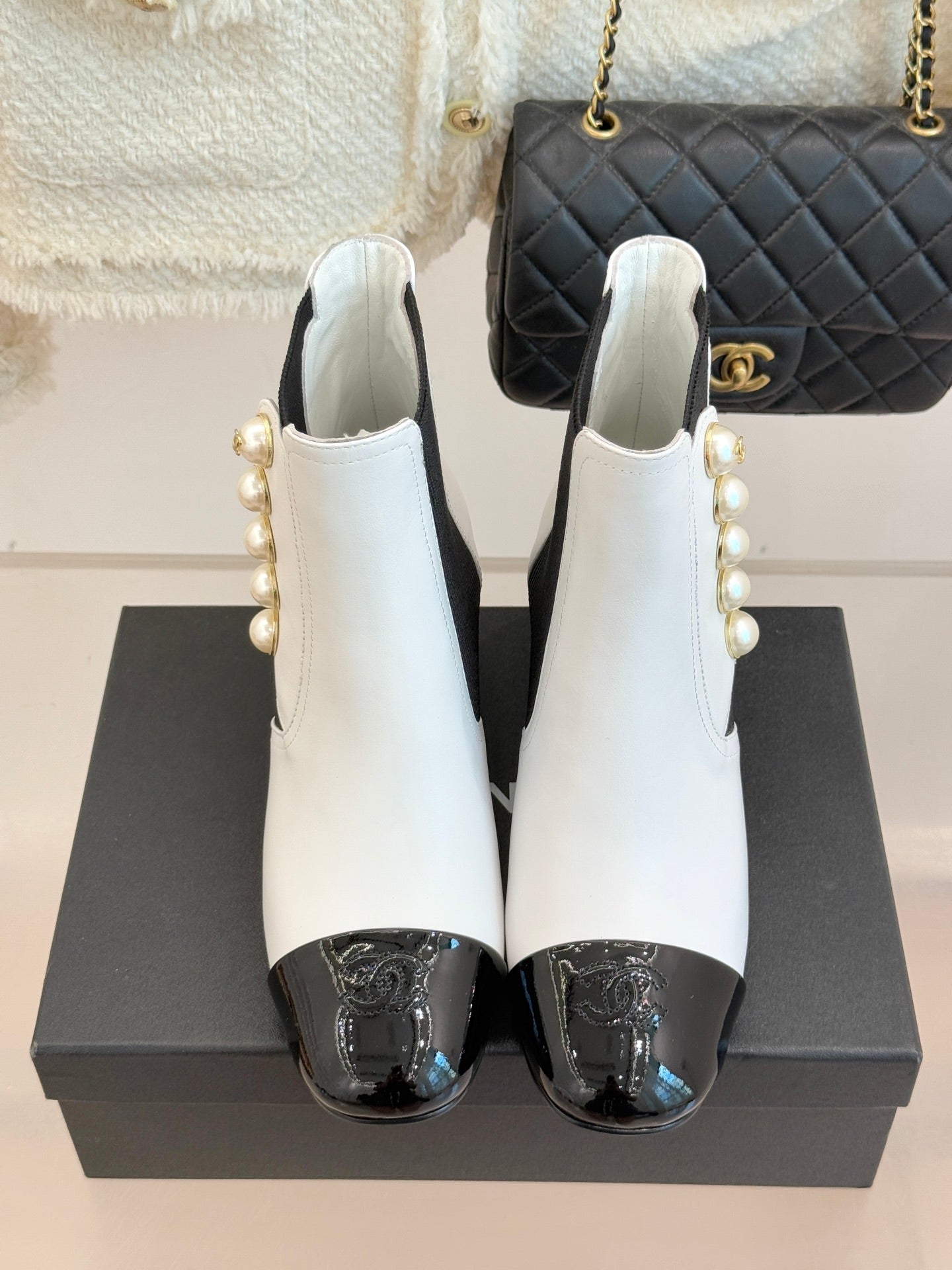 Pair of white ankle boots with black elastic sides, pearl accents, and glossy black toe caps
