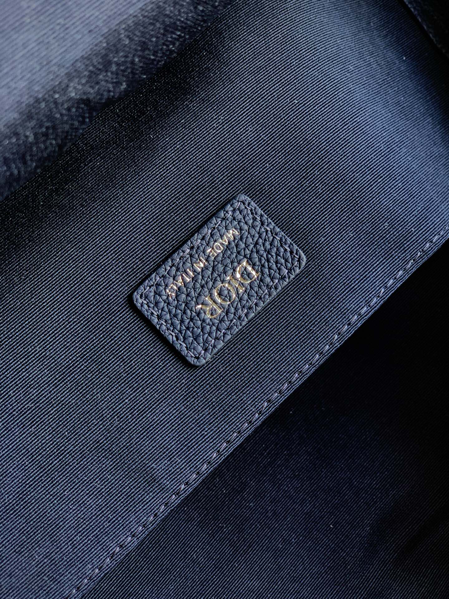 Dior men’s backpack interior close-up with stitched logo patch on dark lining