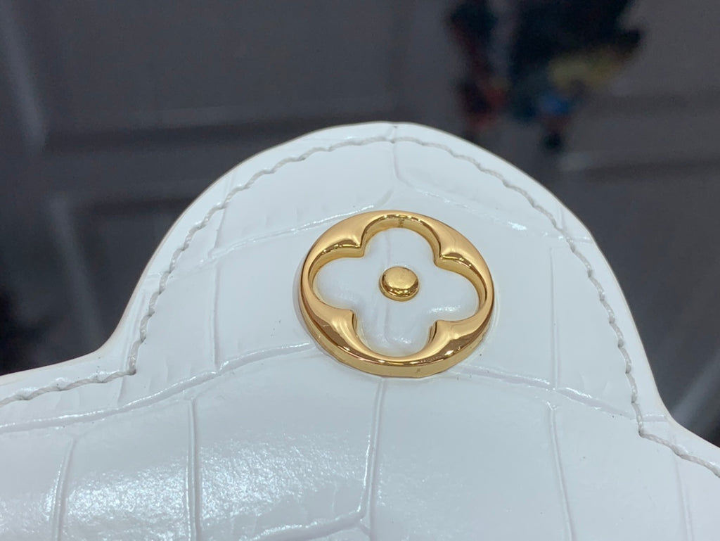 White handbag with gold quatrefoil emblem on flap