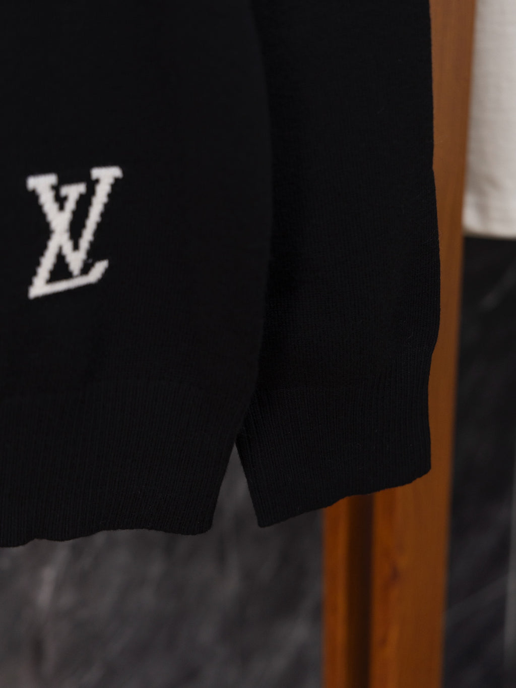 Black sweater sleeve close-up with small white “V” logo