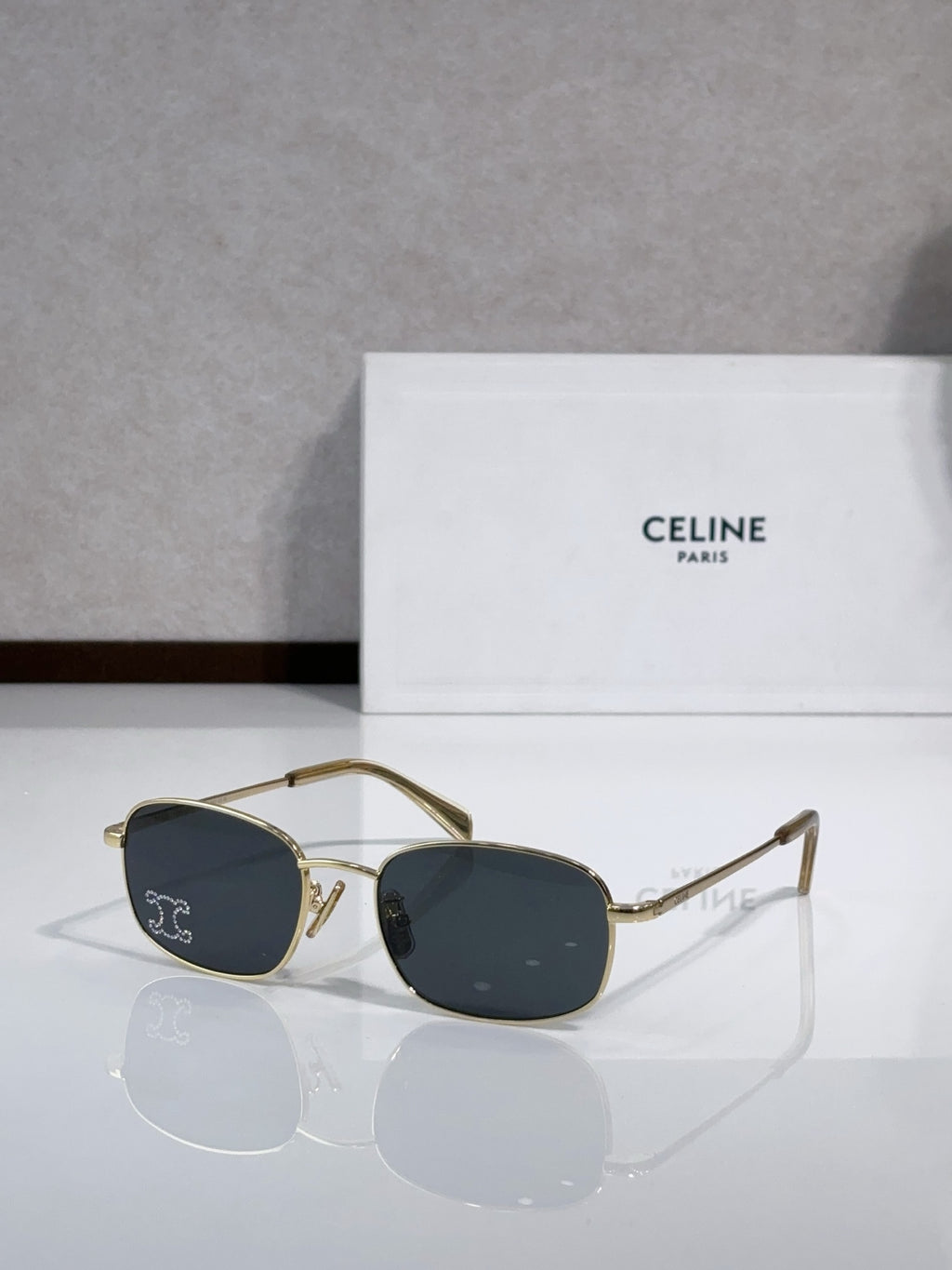 Oval sunglasses with gold-tone frame and dark blue lenses, clear bridge and temples