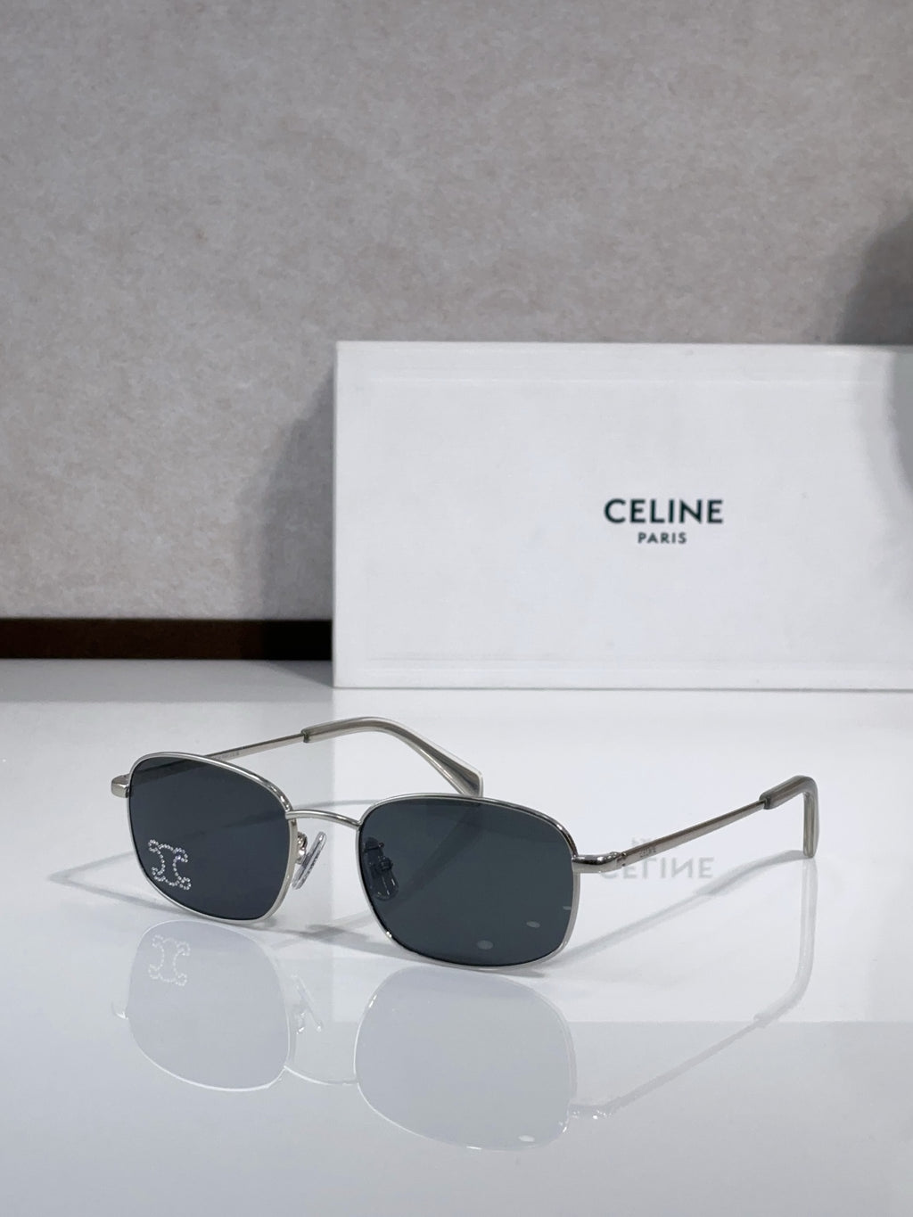 Oval sunglasses with silver-tone frame and dark lenses, curved temple with logo