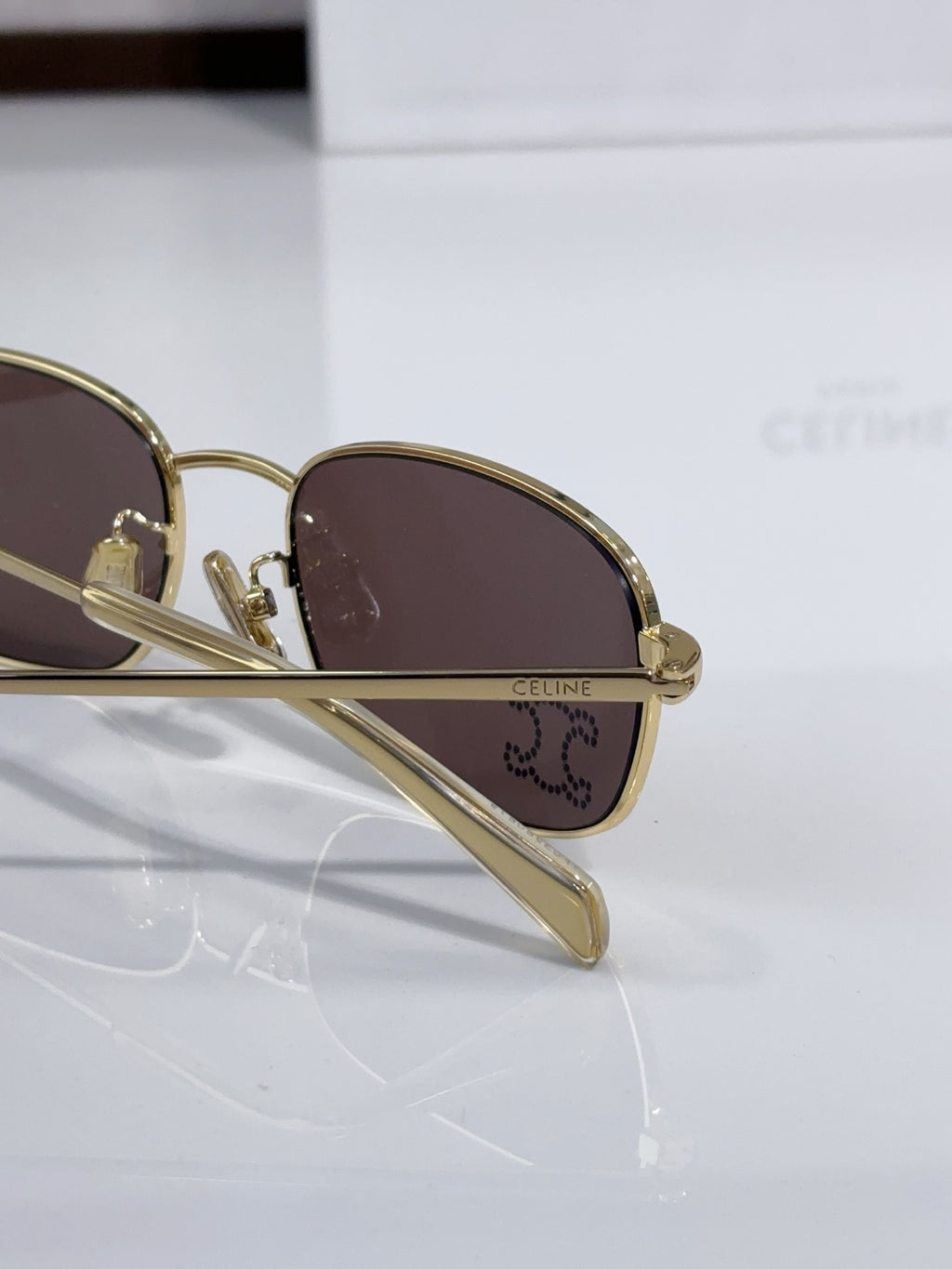 Side view of oval sunglasses with gold-tone frame and dark brown lens, logo on temple