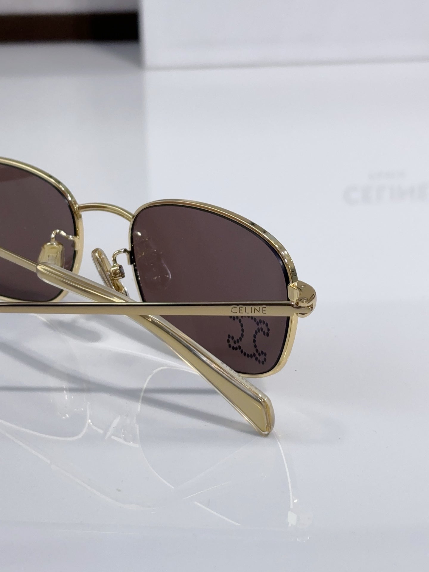 Side view of oval sunglasses with gold-tone frame and dark brown lens, logo on temple