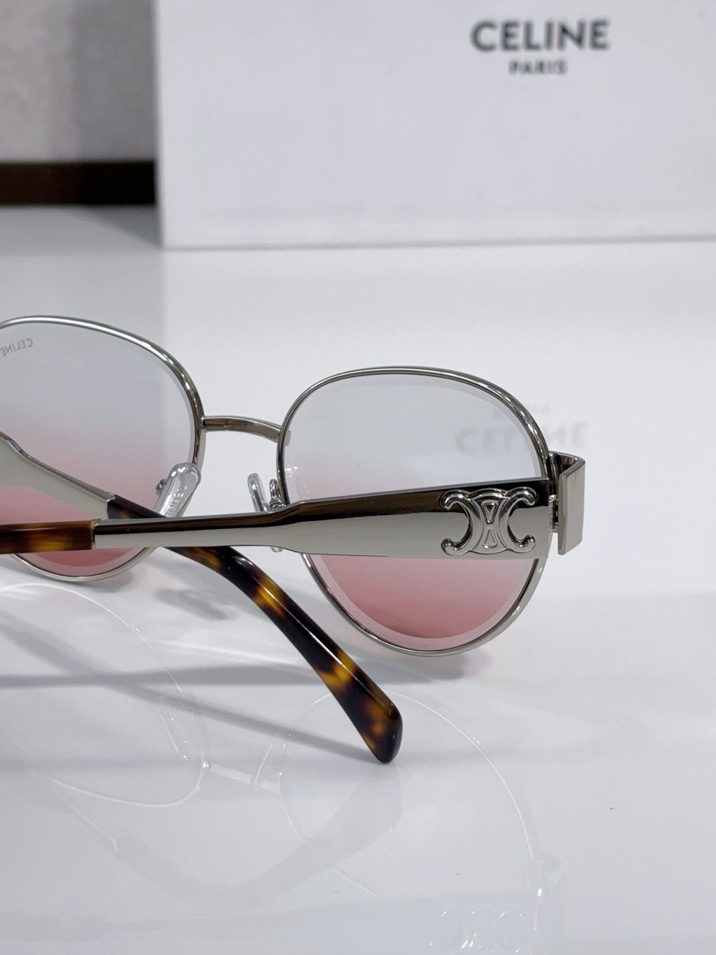 Round sunglasses close-up with silver frame, pink-tinted lenses, engraved hinge detail