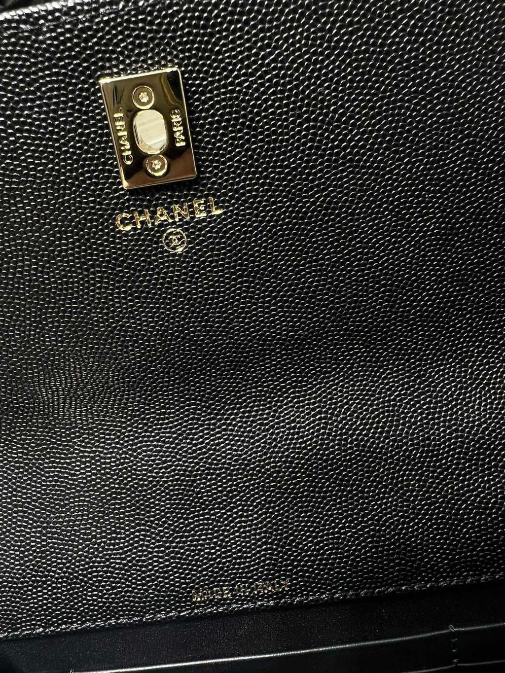 Textured black Chanel bag close-up with gold logo plate and CC charm