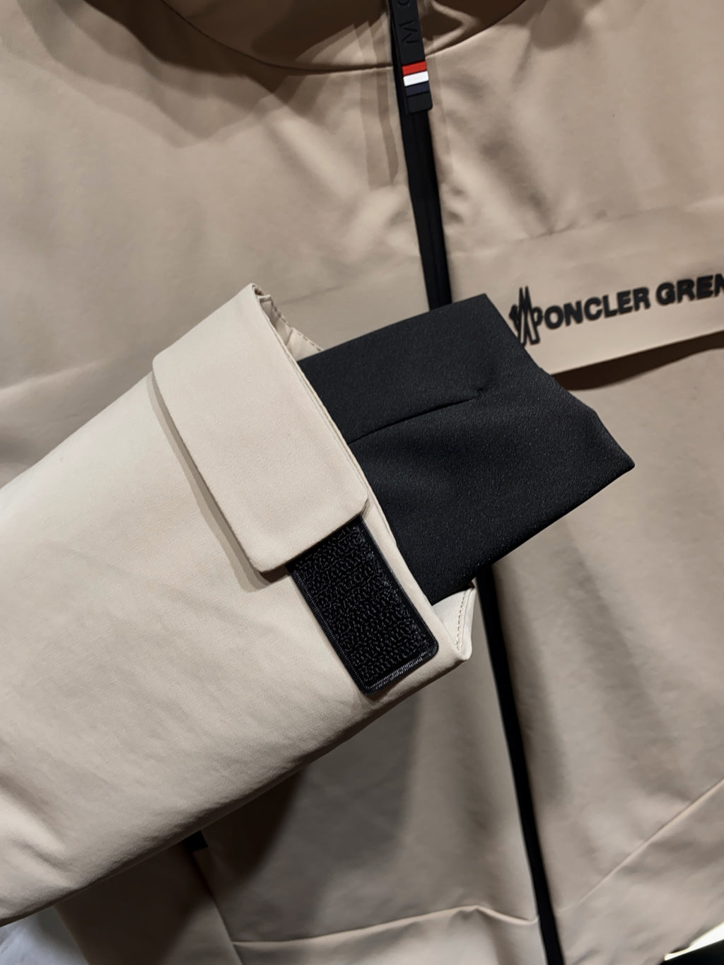 Beige hooded jacket with black-trim pocket and adjustable cuff strap