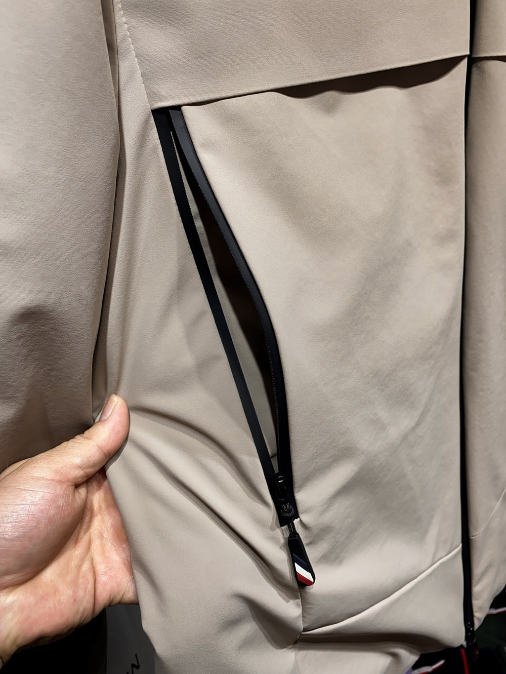 Beige zip-front jacket with black piping and angled inner pocket