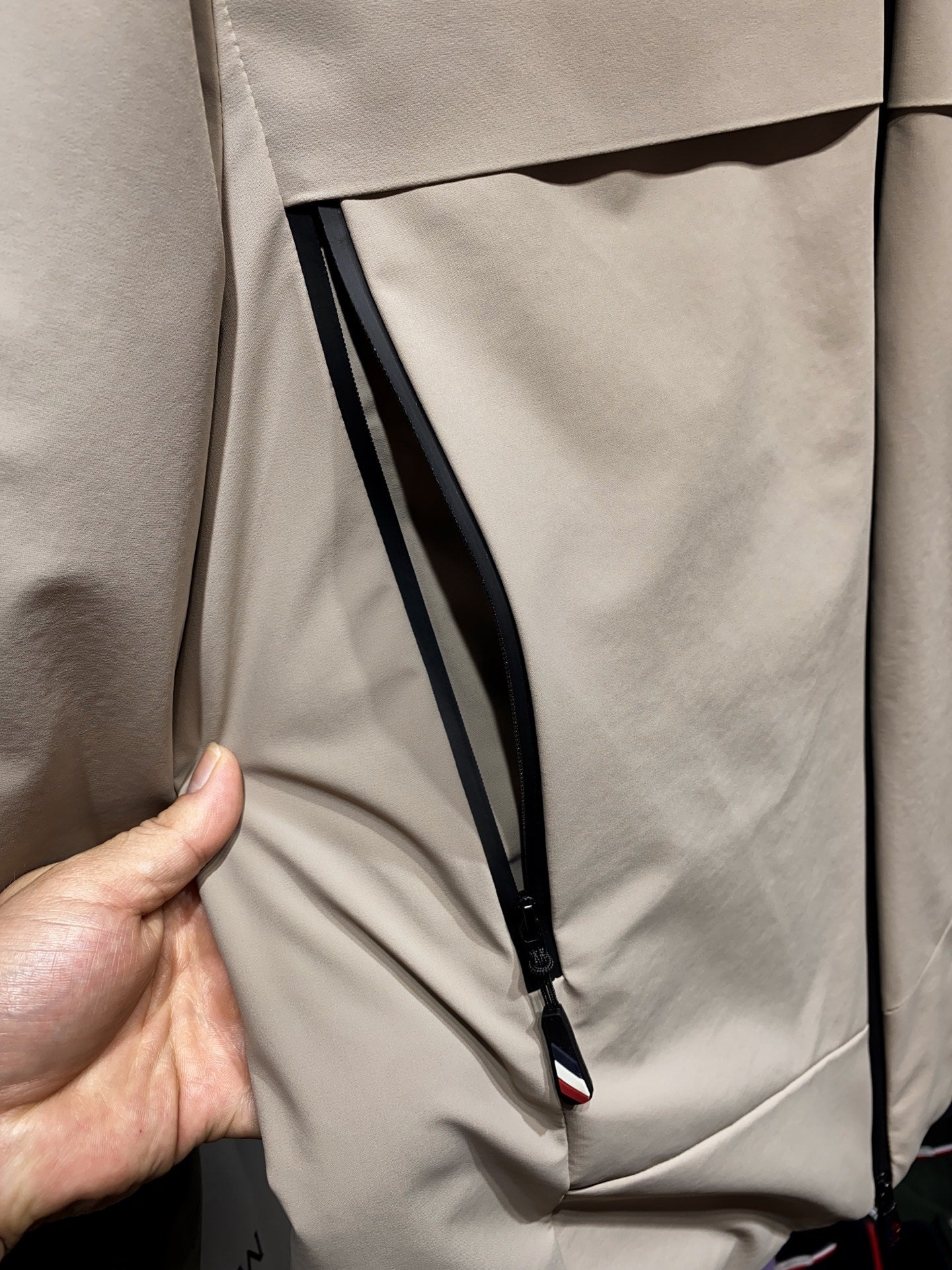 Beige zip-front jacket with black piping and angled inner pocket