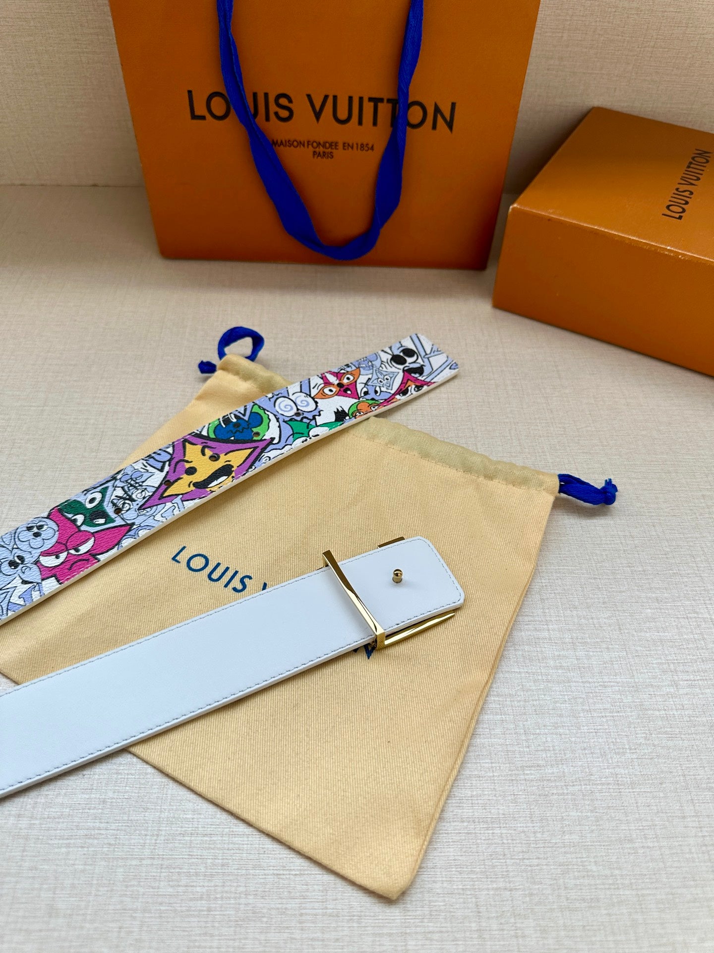 Louis Vuitton belt with white cartoon strap, gold buckle, and tan dust bag included