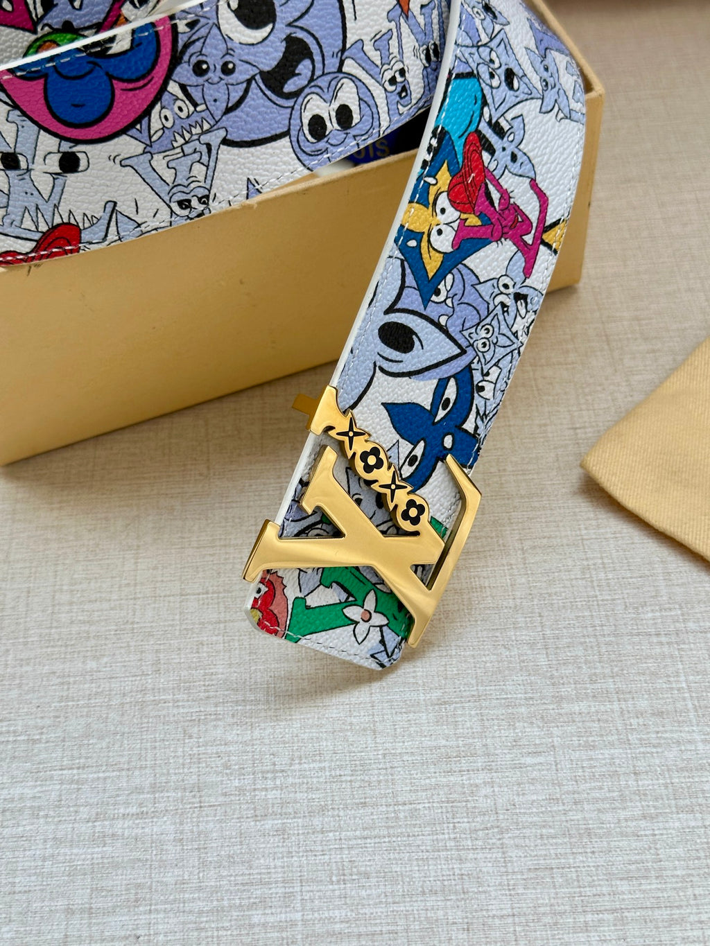 Louis Vuitton belt buckle and strap end in view; gold hardware on cartoon print