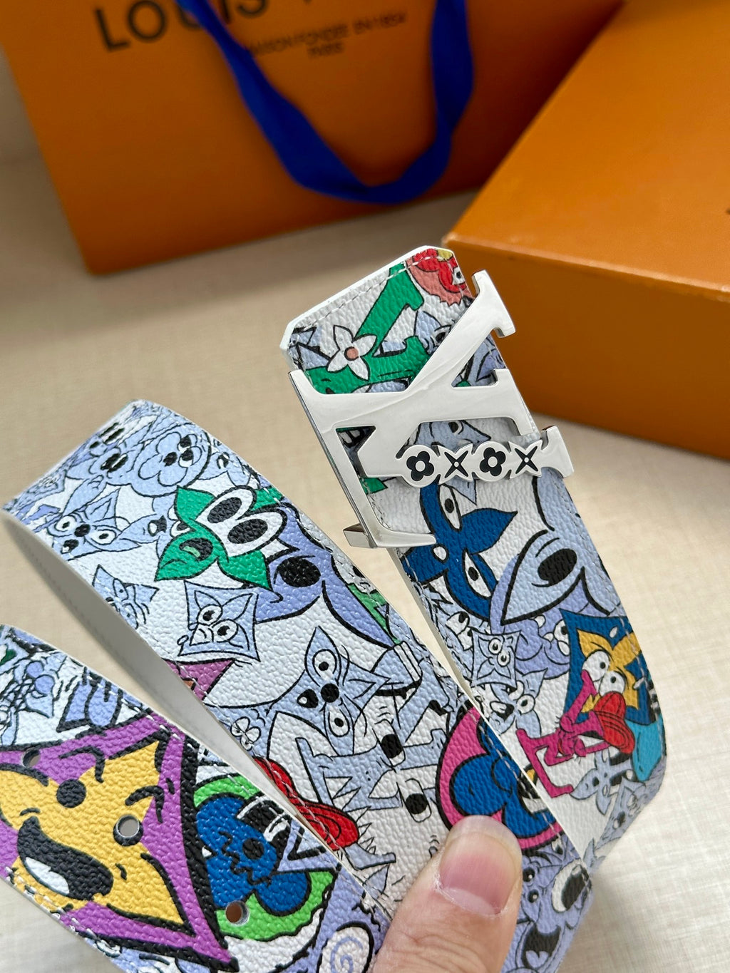 Louis Vuitton belt buckle close-up on white strap with colorful cartoon print