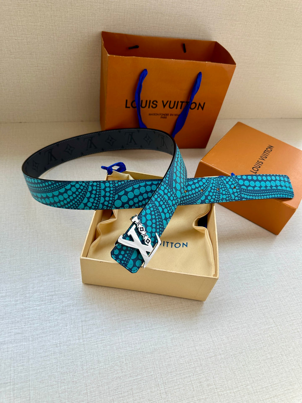 Turquoise dotted belt with gold LV buckle beside a beige dust pouch