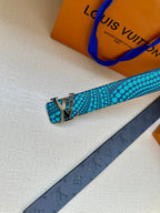 Turquoise dotted belt with gold-tone hardware laid over a dark monogram strap