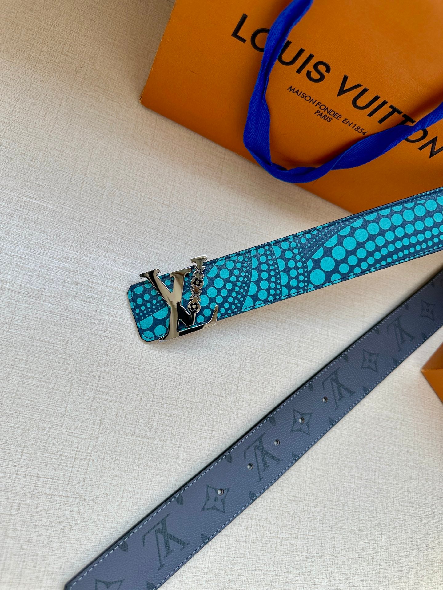 Turquoise dotted belt with gold-tone hardware laid over a dark monogram strap