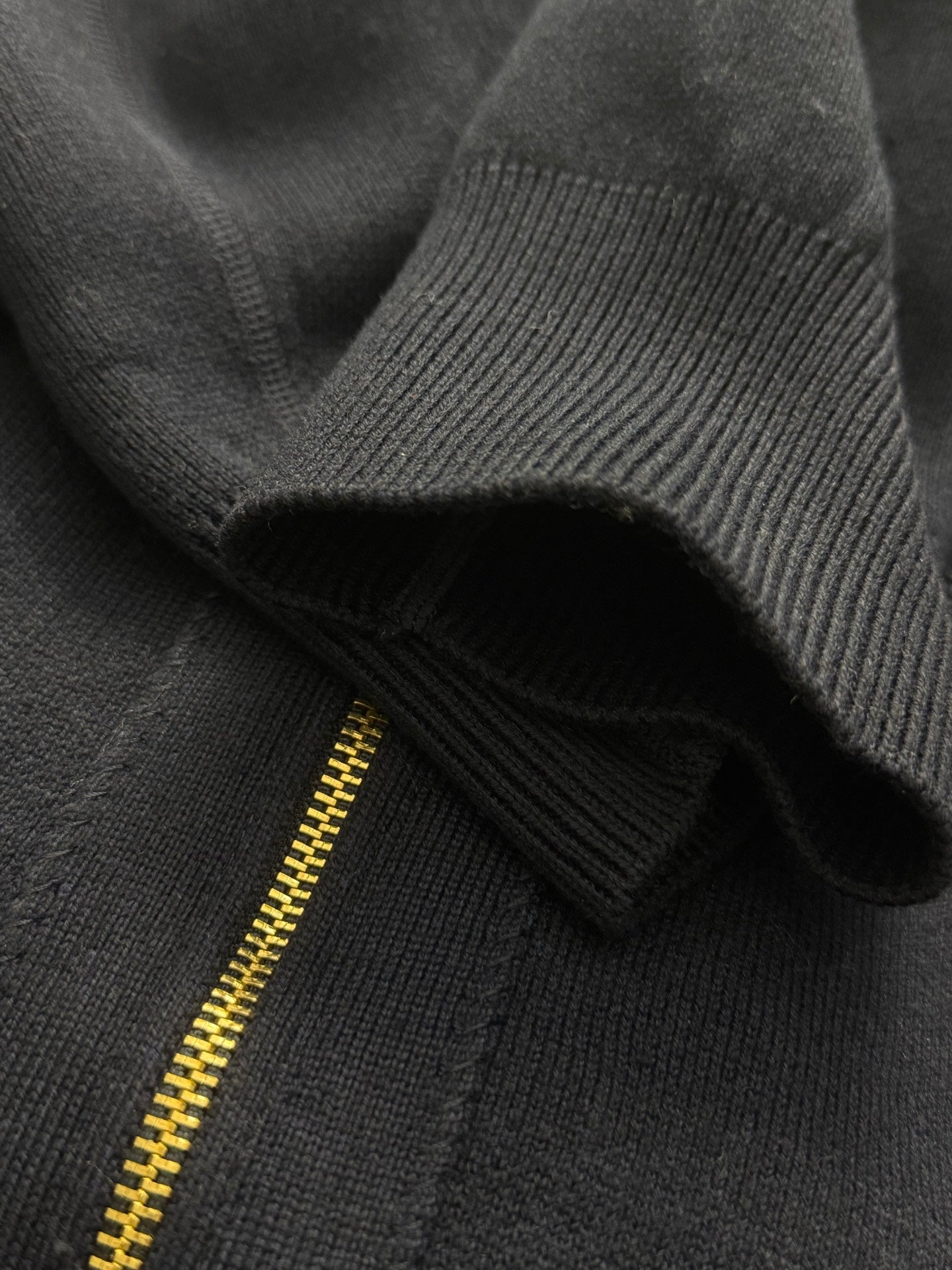 Close-up of dark knit hoodie fabric with gold zipper edge and ribbed trim