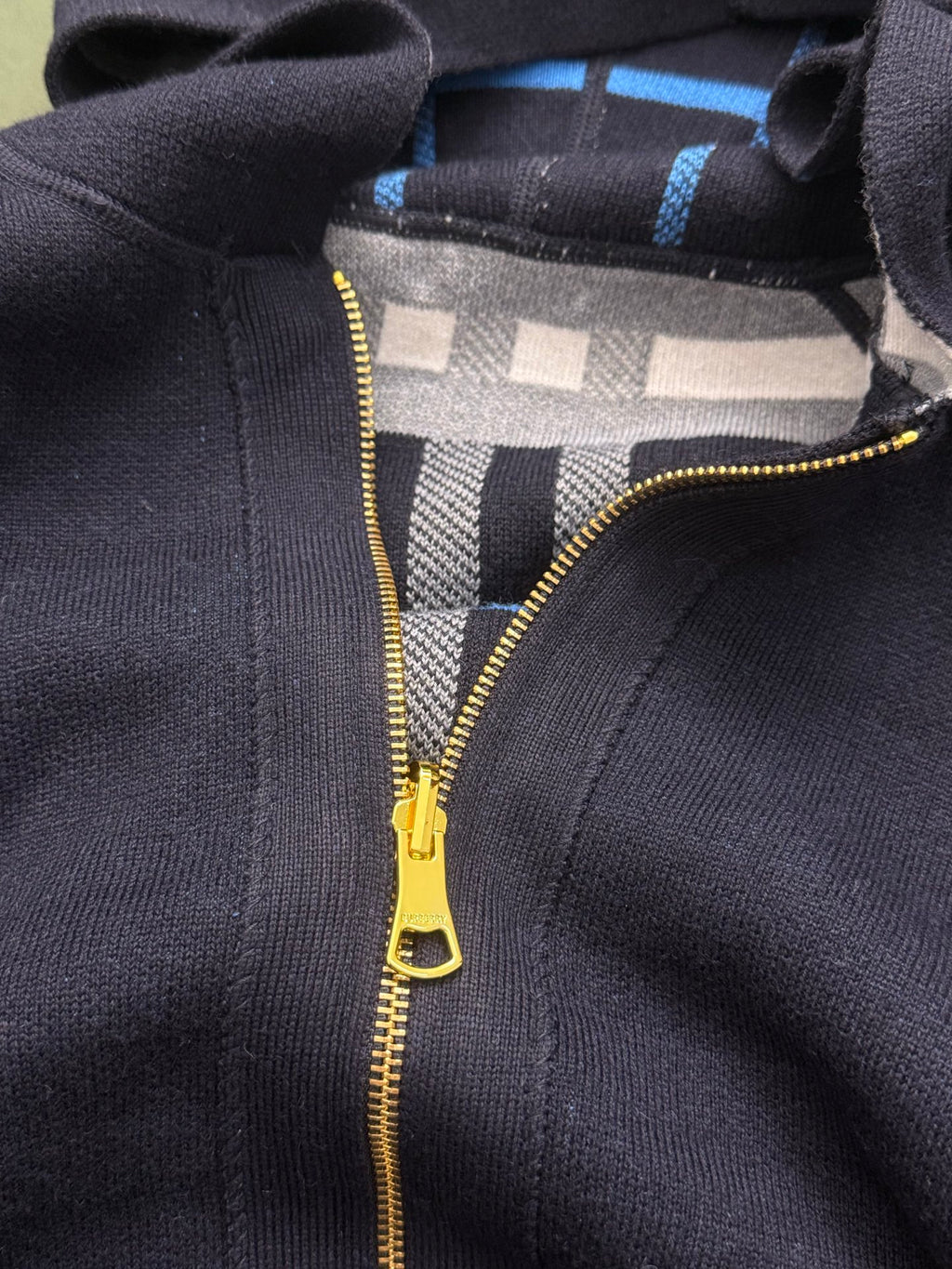 Close-up of navy Burberry hoodie with gold zipper and plaid lining under hood