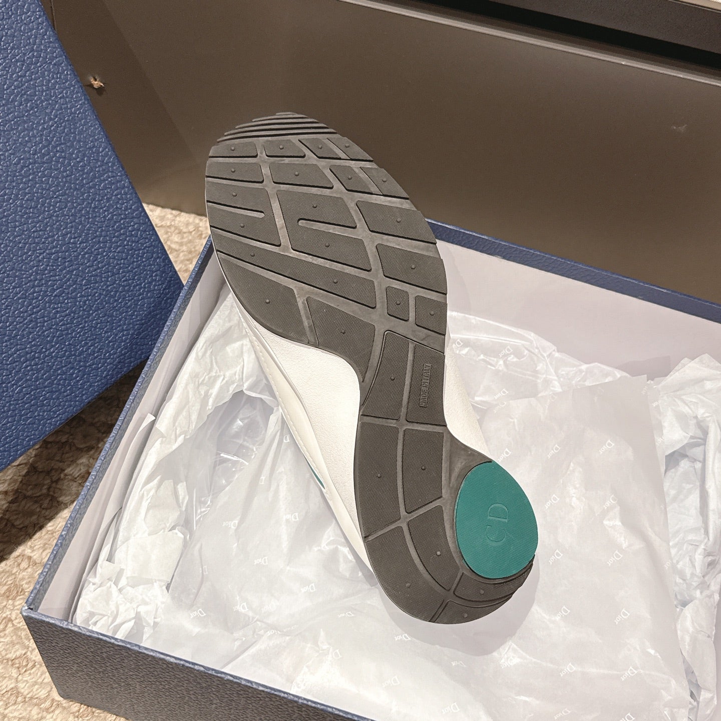 Unisex sneaker outsole in box, dark tread with white midsole and teal heel insert