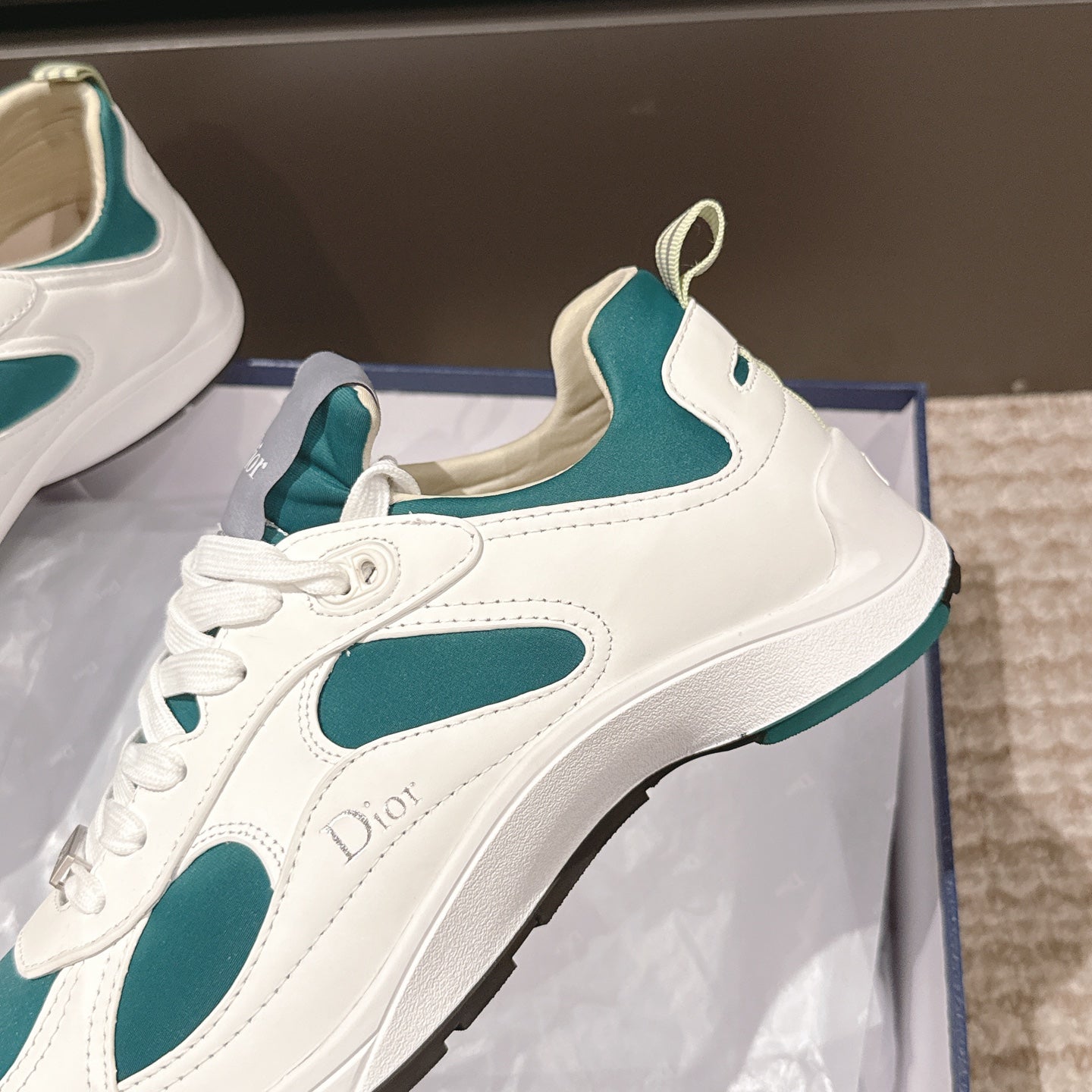 Unisex sneaker close-up, white upper with teal panel and Dior logo on side