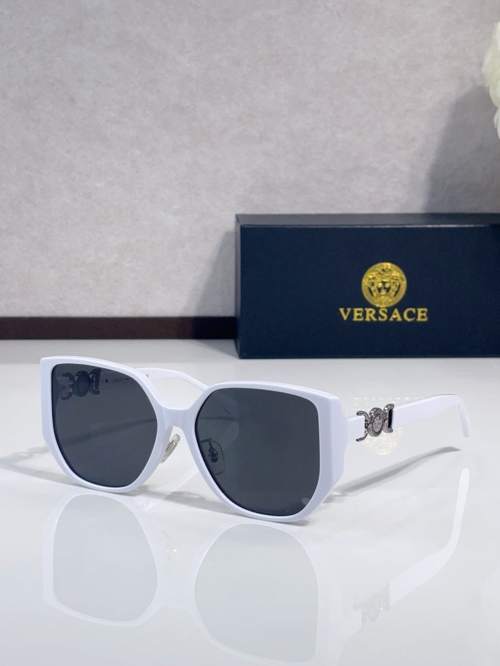 White sunglasses with rounded dark lenses and gold logo detail on temples