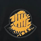 Black Moncler long-sleeve top close-up of yellow circular logo embroidery