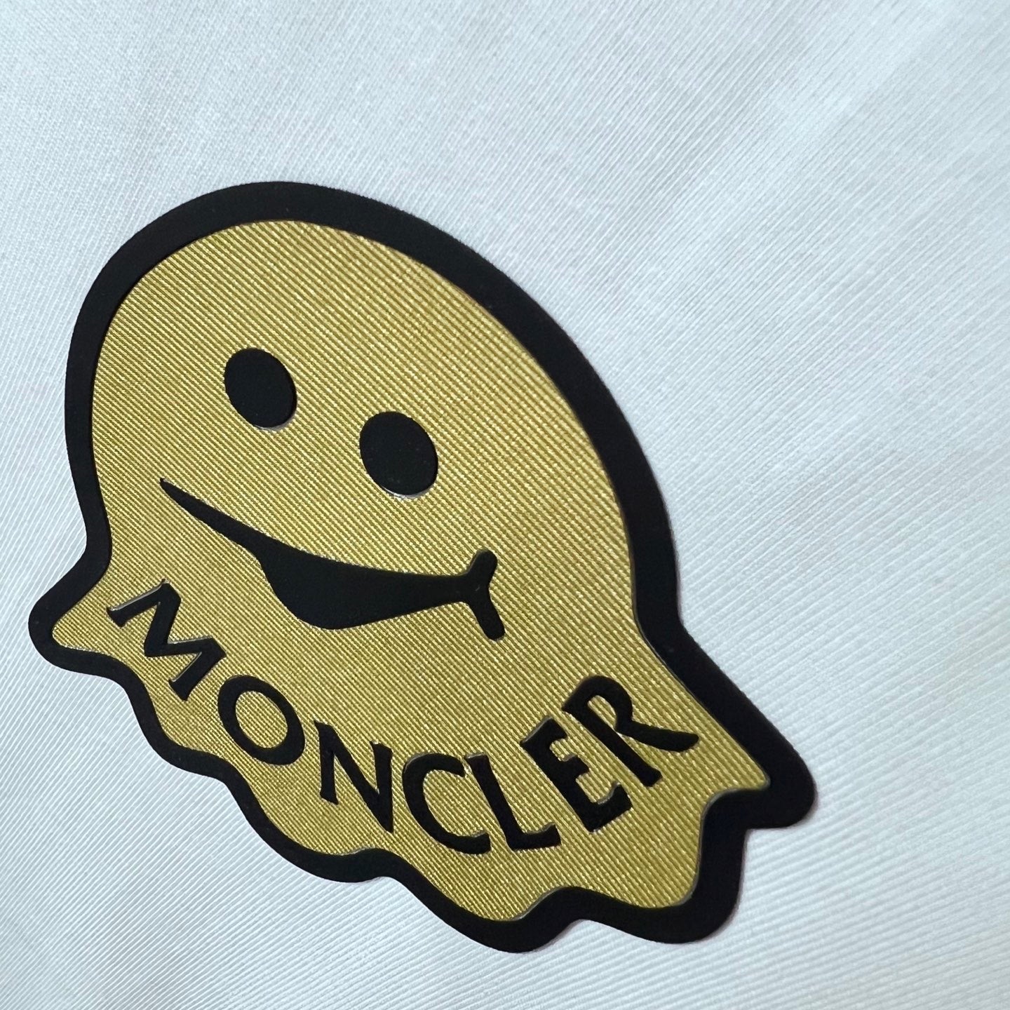 Moncler smile emblem patch on white fabric with embroidered-style text