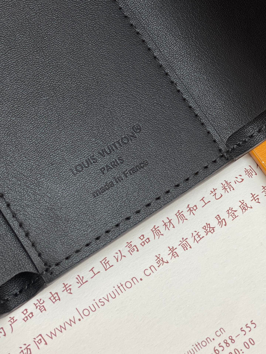 Black textured leather small bag corner with embossed logo and contrast stitching.