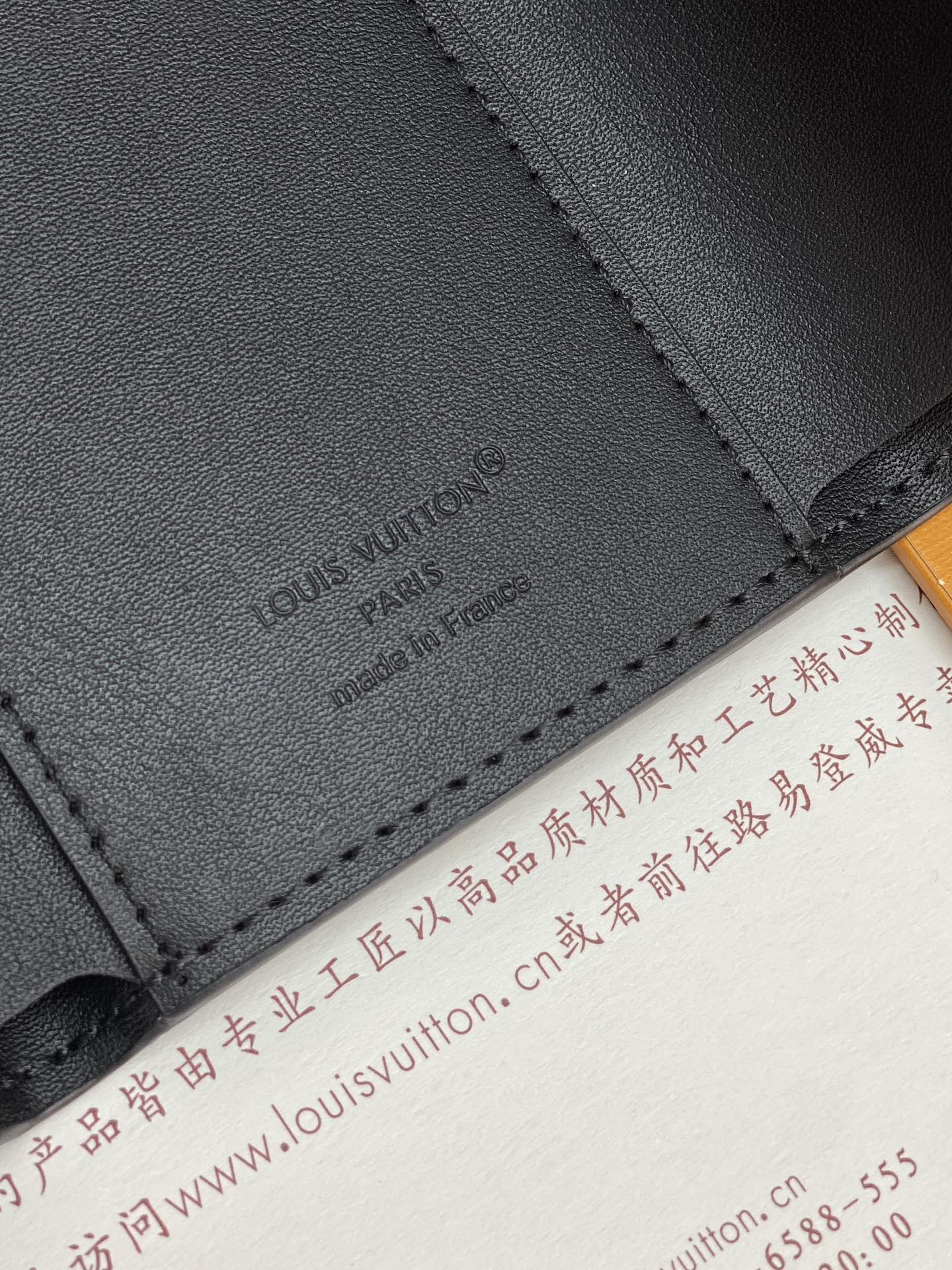 Black textured leather small bag corner with embossed logo and contrast stitching.