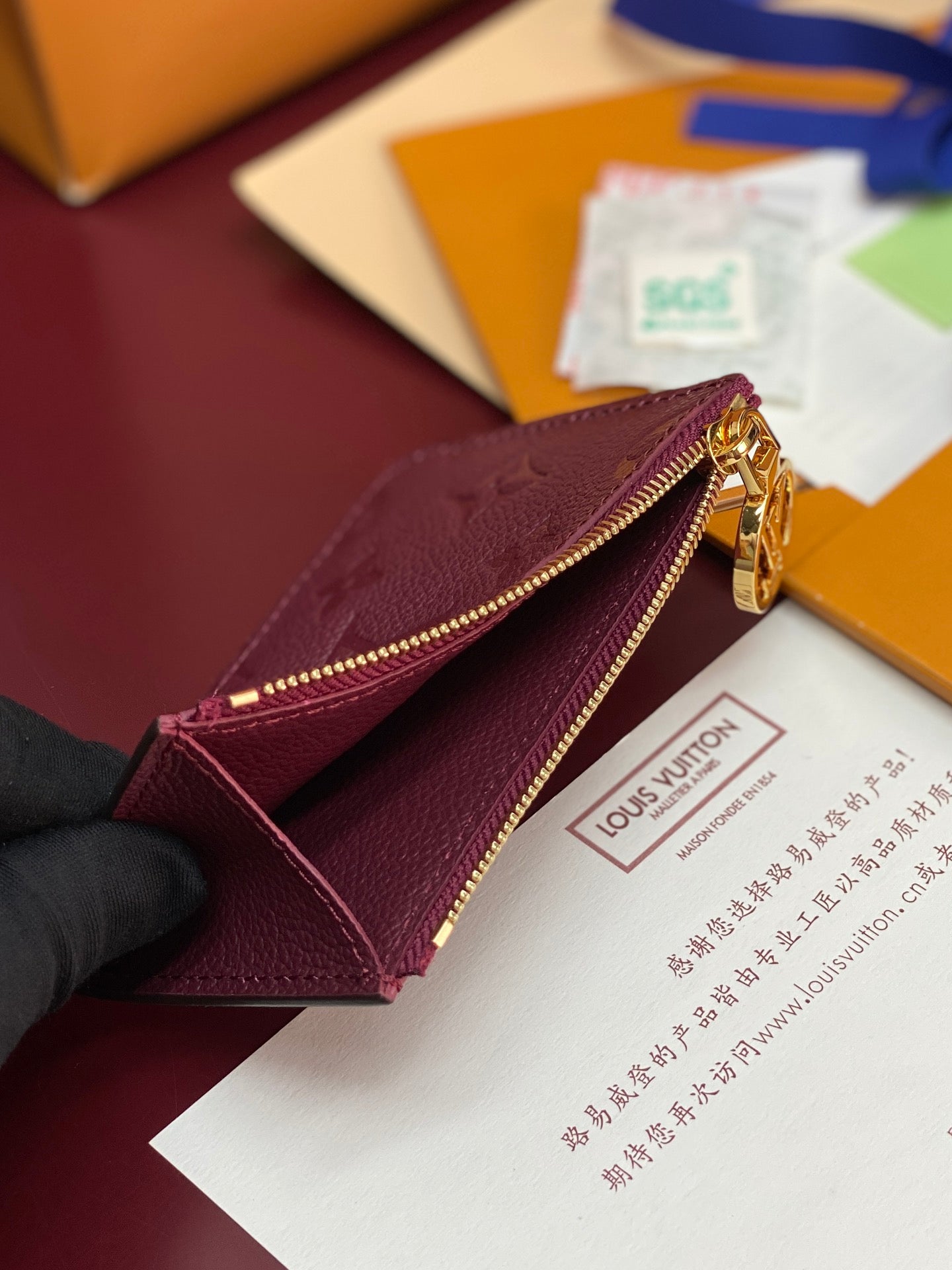 Small leather pouch bag with burgundy interior, open zipper, and gold-tone hardware