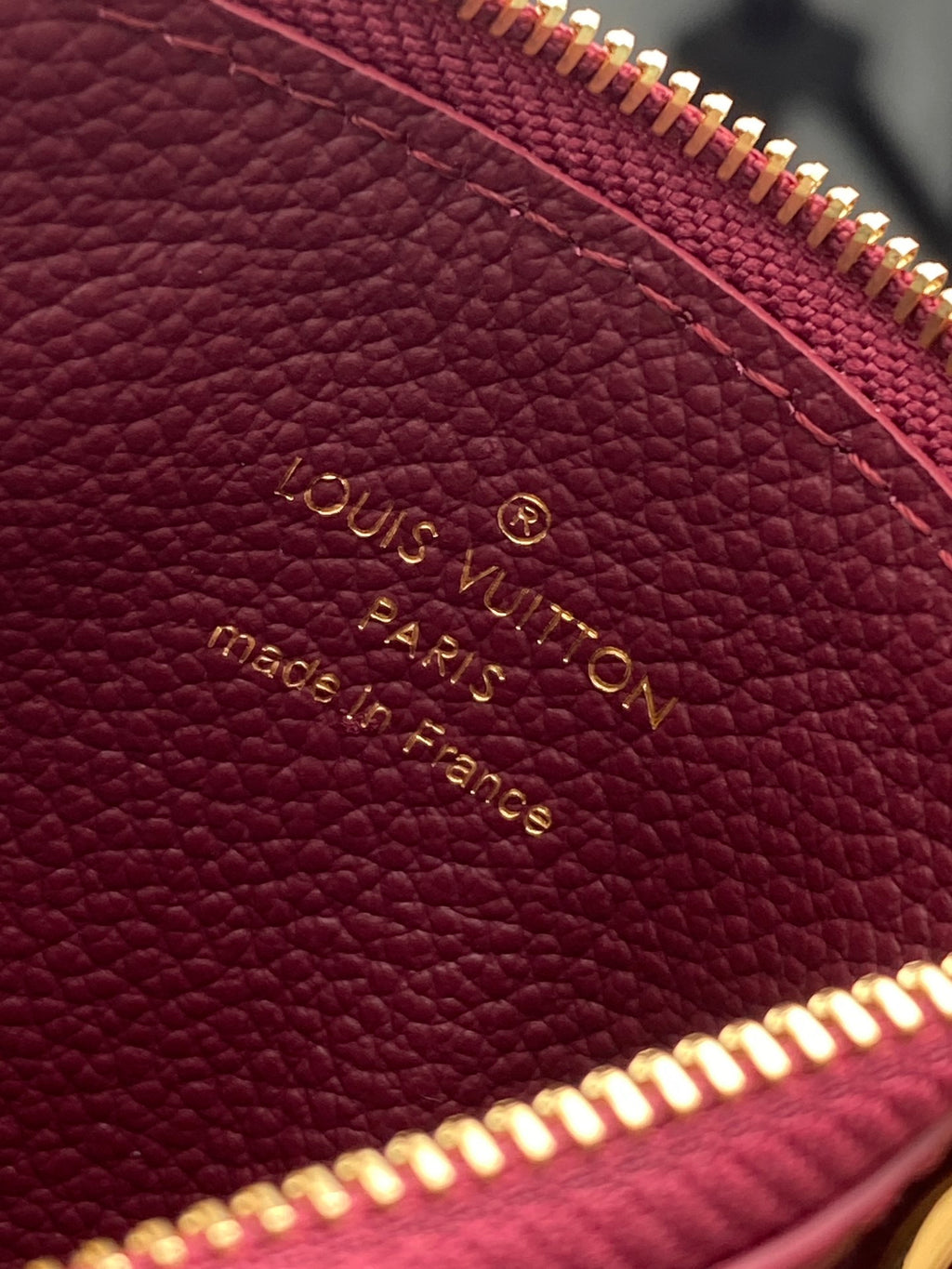 Burgundy Louis Vuitton monogram leather pouch with embossed text and gold zipper