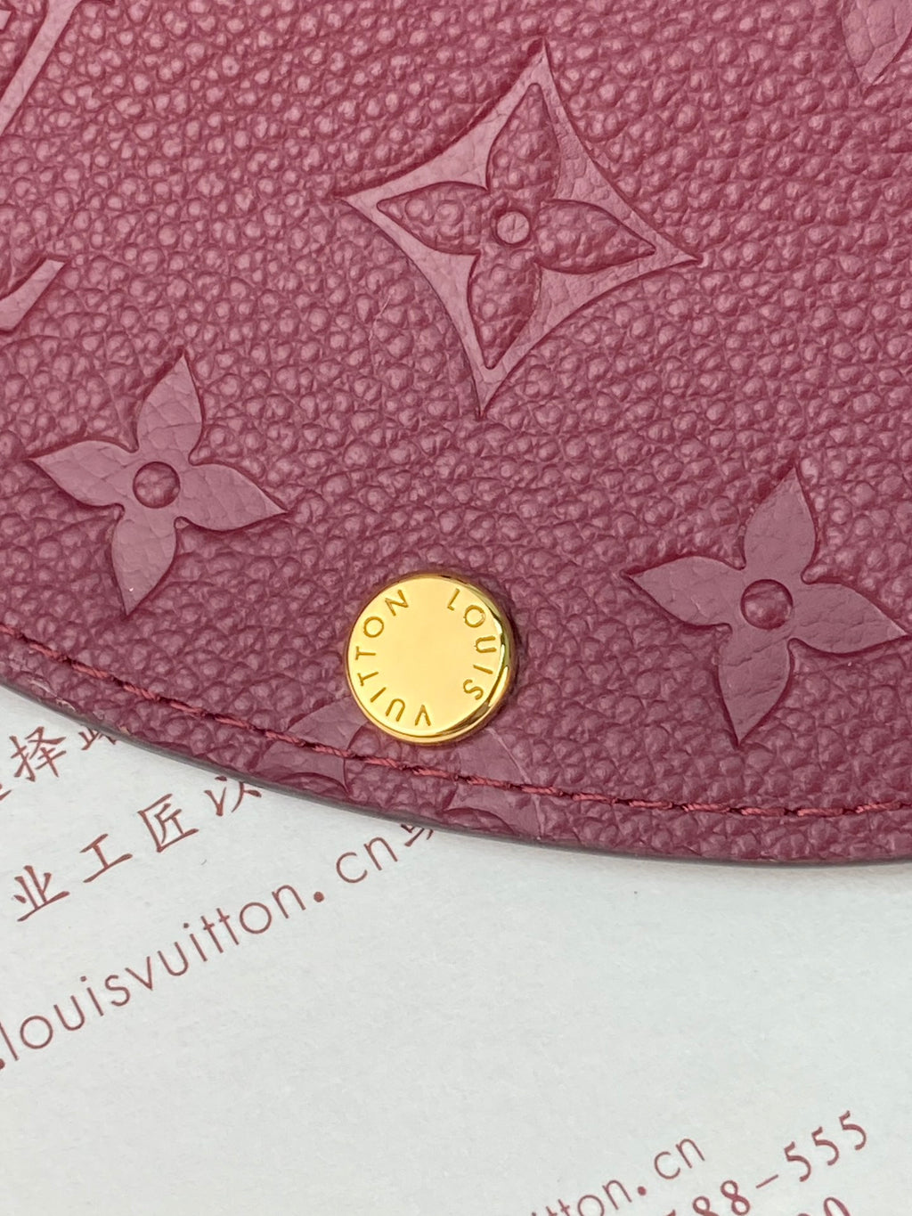 Small Louis Vuitton monogram bag close-up with gold snap and embossed flower motifs, dark plum
