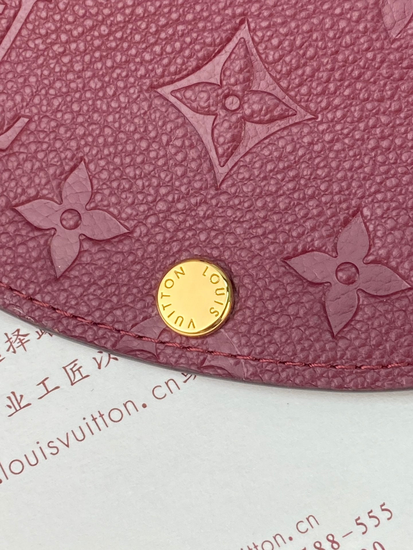 Small Louis Vuitton monogram bag close-up with gold snap and embossed flower motifs, dark plum