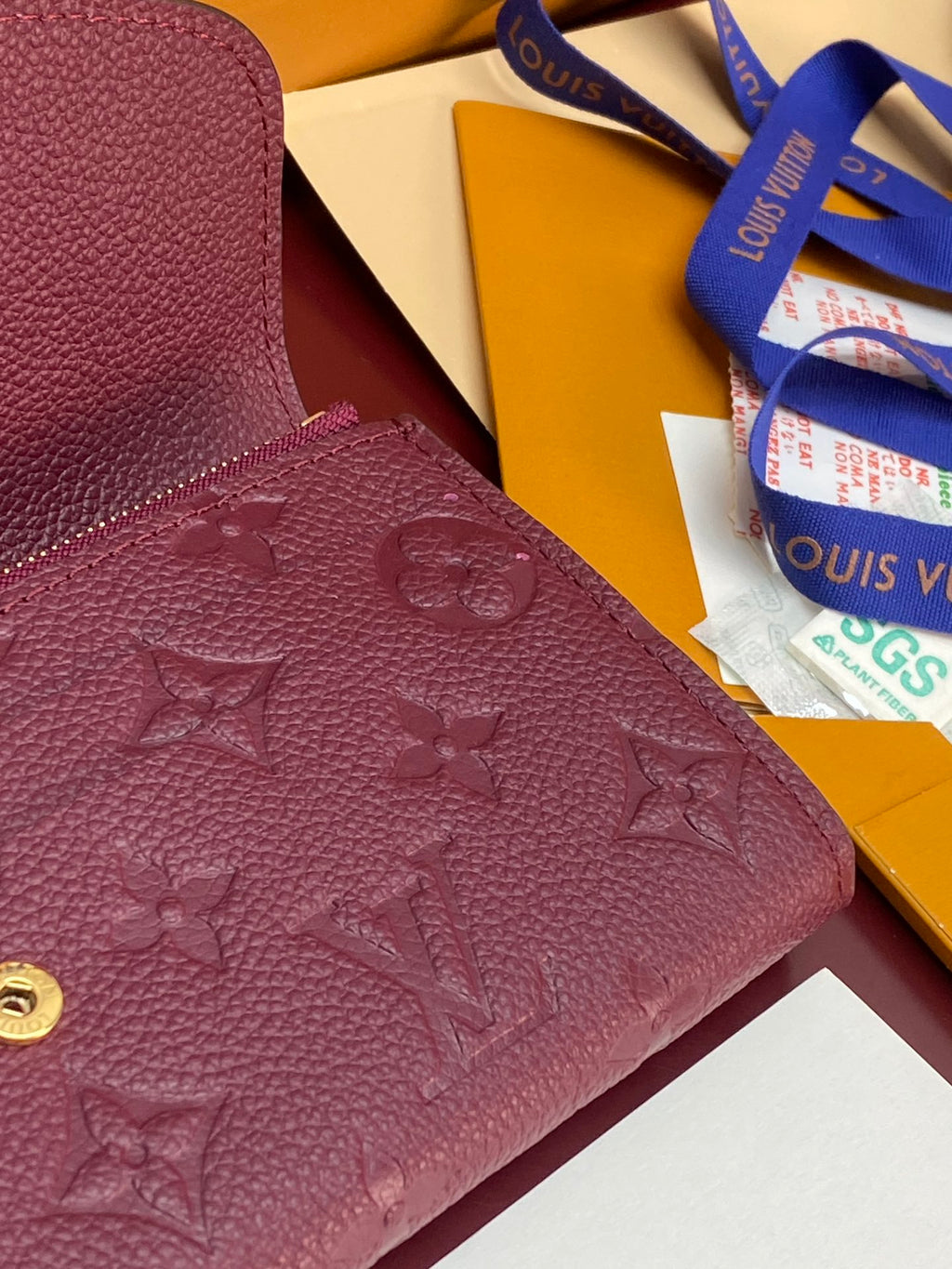 Small bag corner close-up showing burgundy/purple embossed monogram and gold snap.