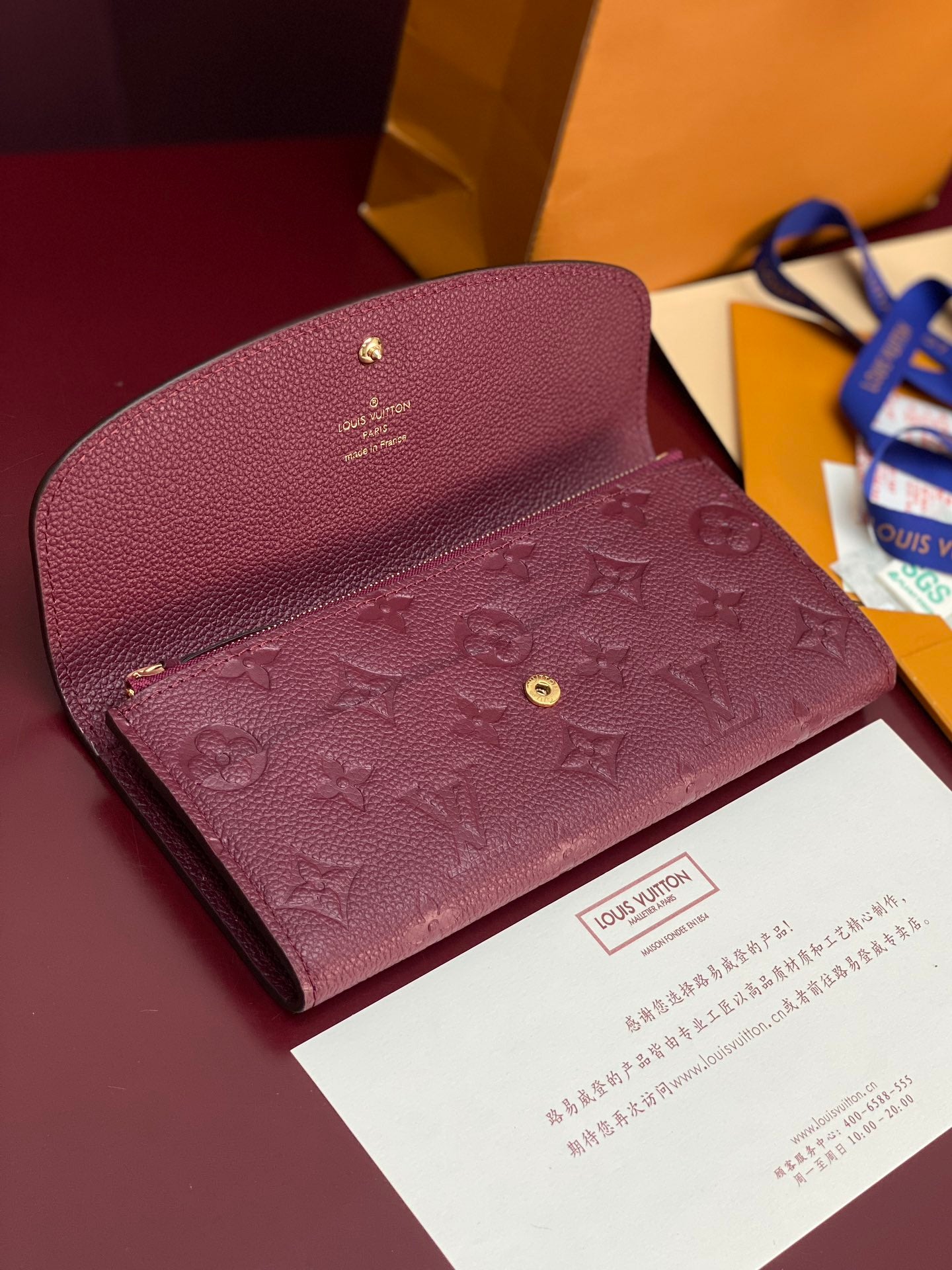 Small bag with flap and burgundy/purple embossed monogram, visible gold snap hardware.