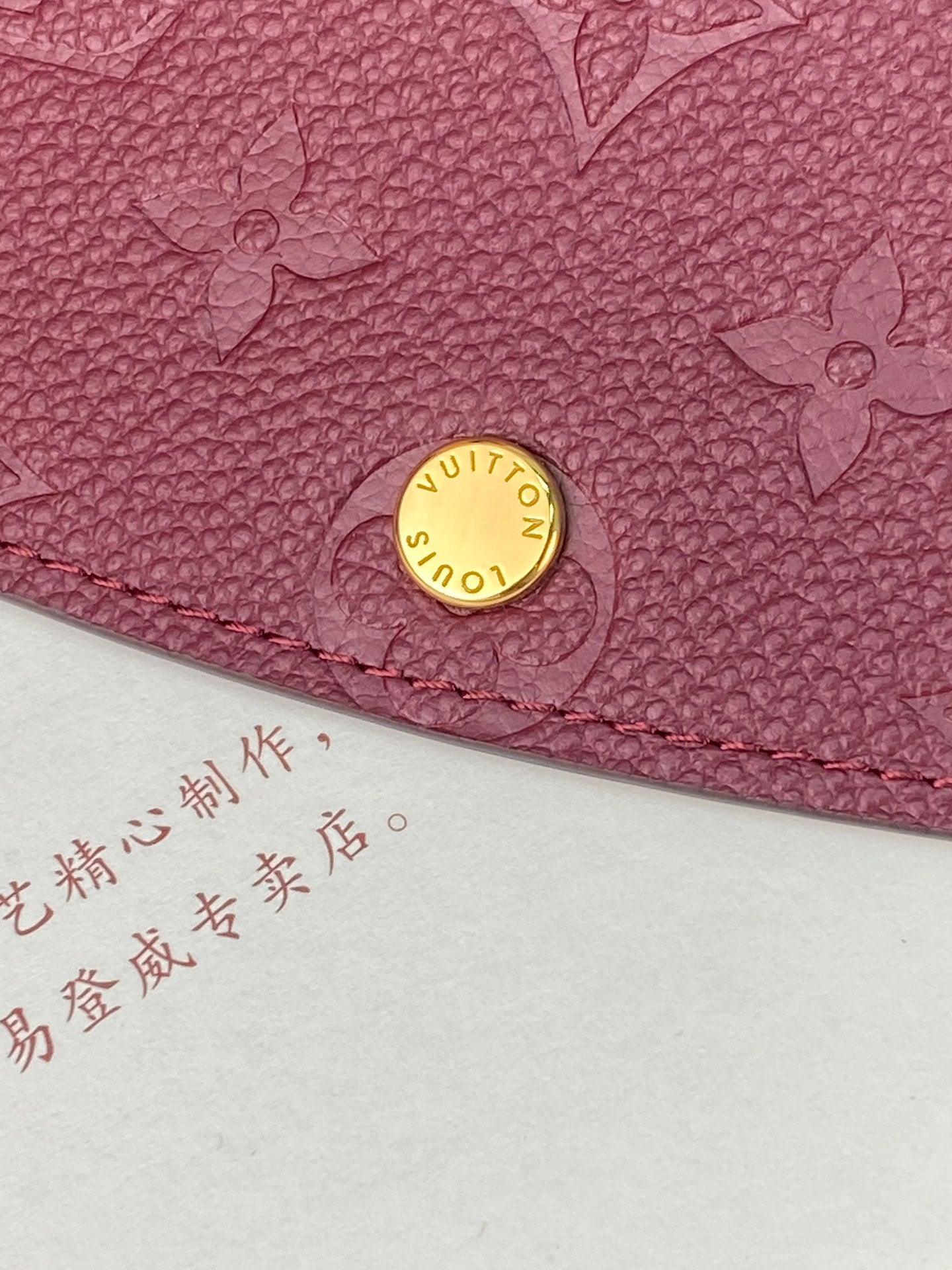 Small bag close-up of gold Louis Vuitton button and burgundy/purple embossed leather edge.