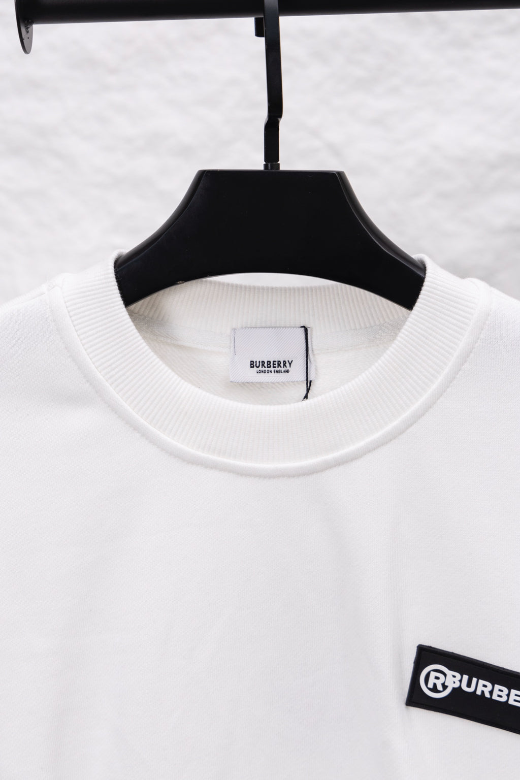 White crewneck sweatshirt with ribbed neckline and black logo patch