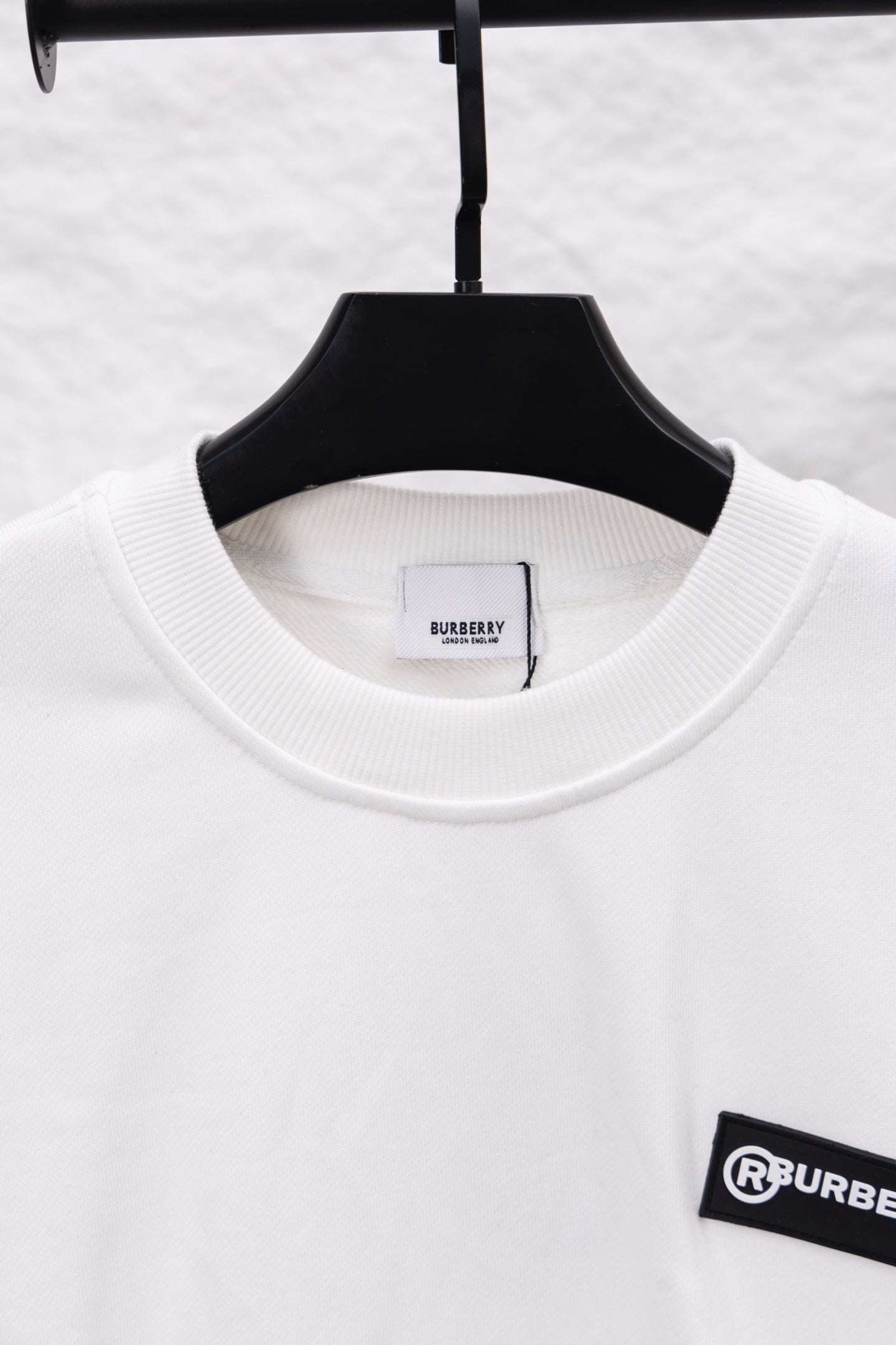 White crewneck sweatshirt with ribbed neckline and black logo patch