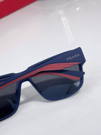 Prada sunglasses side view, navy frame with red stripe and PRADA logo on temple