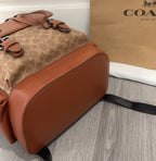 Coach backpack bottom/side view with brown leather base and black crossbody strap