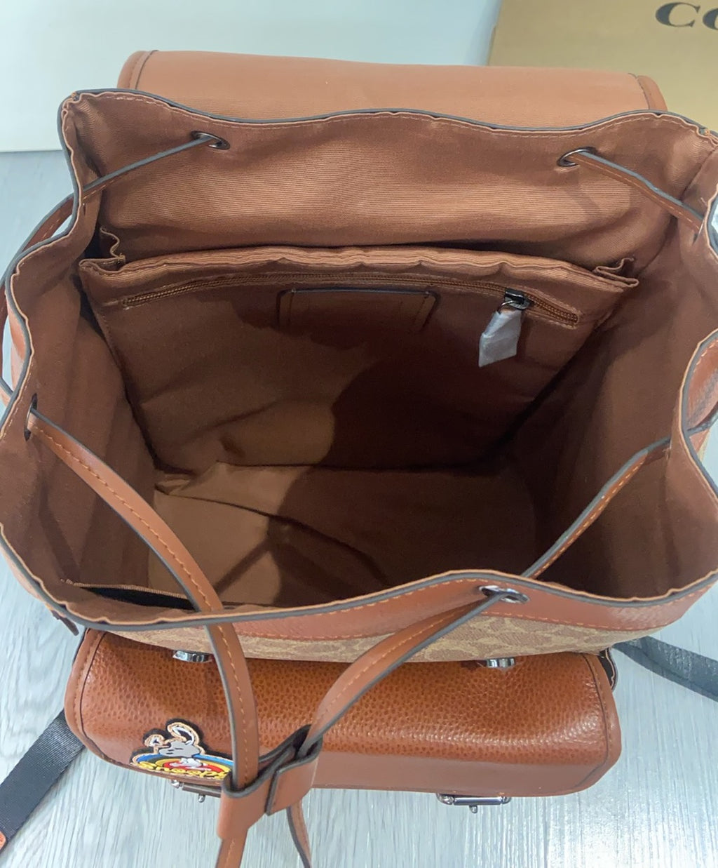 Coach backpack interior view with open top, tan lining, handles, and zipper pocket
