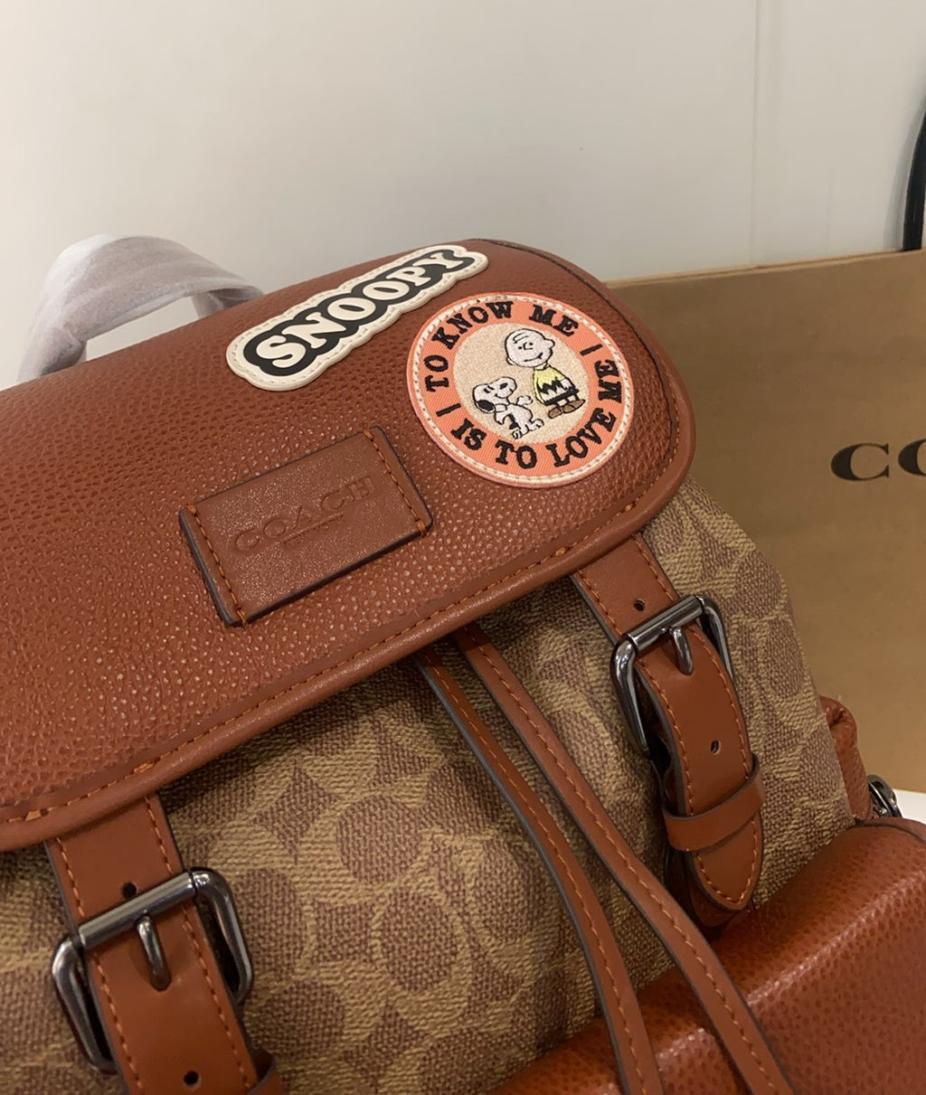 Coach backpack close-up of top flap with Snoopy emblem and tan monogram backing