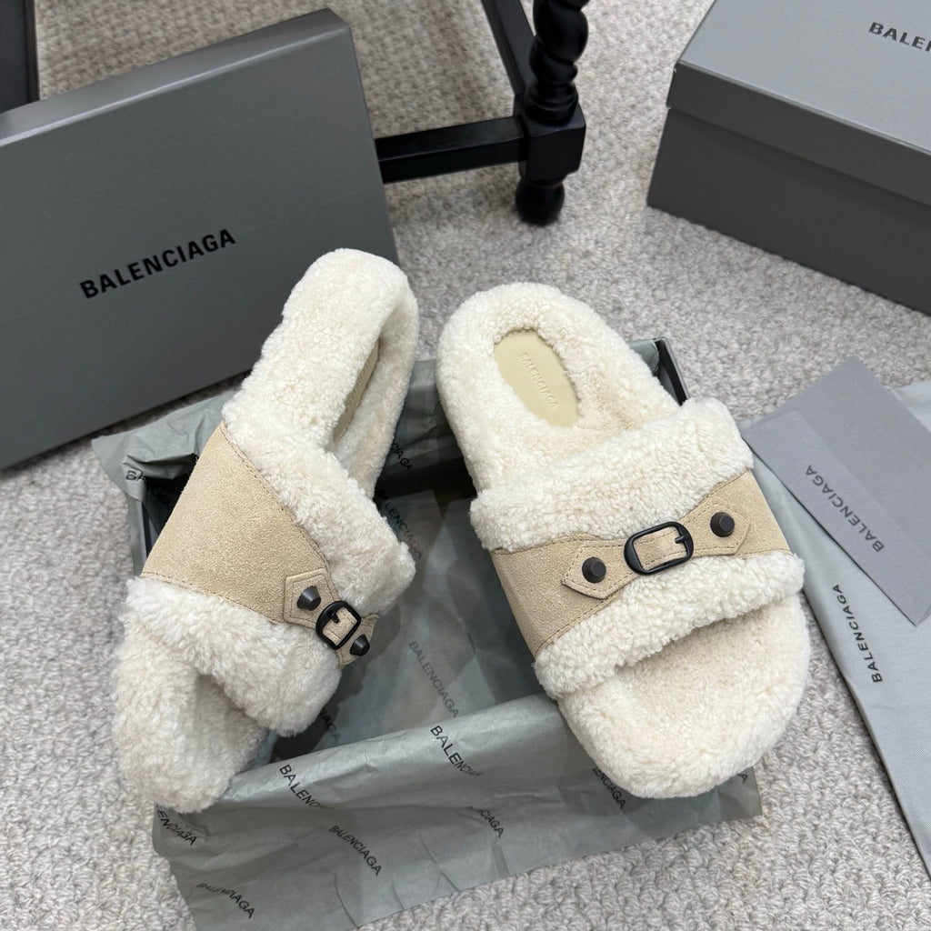 Pair of cream shearling sandals with tan side straps and black buckle details.